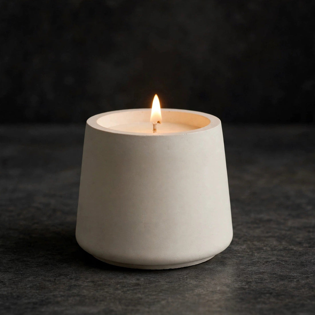 Lit soy candle in a white trapezoid concrete vessel